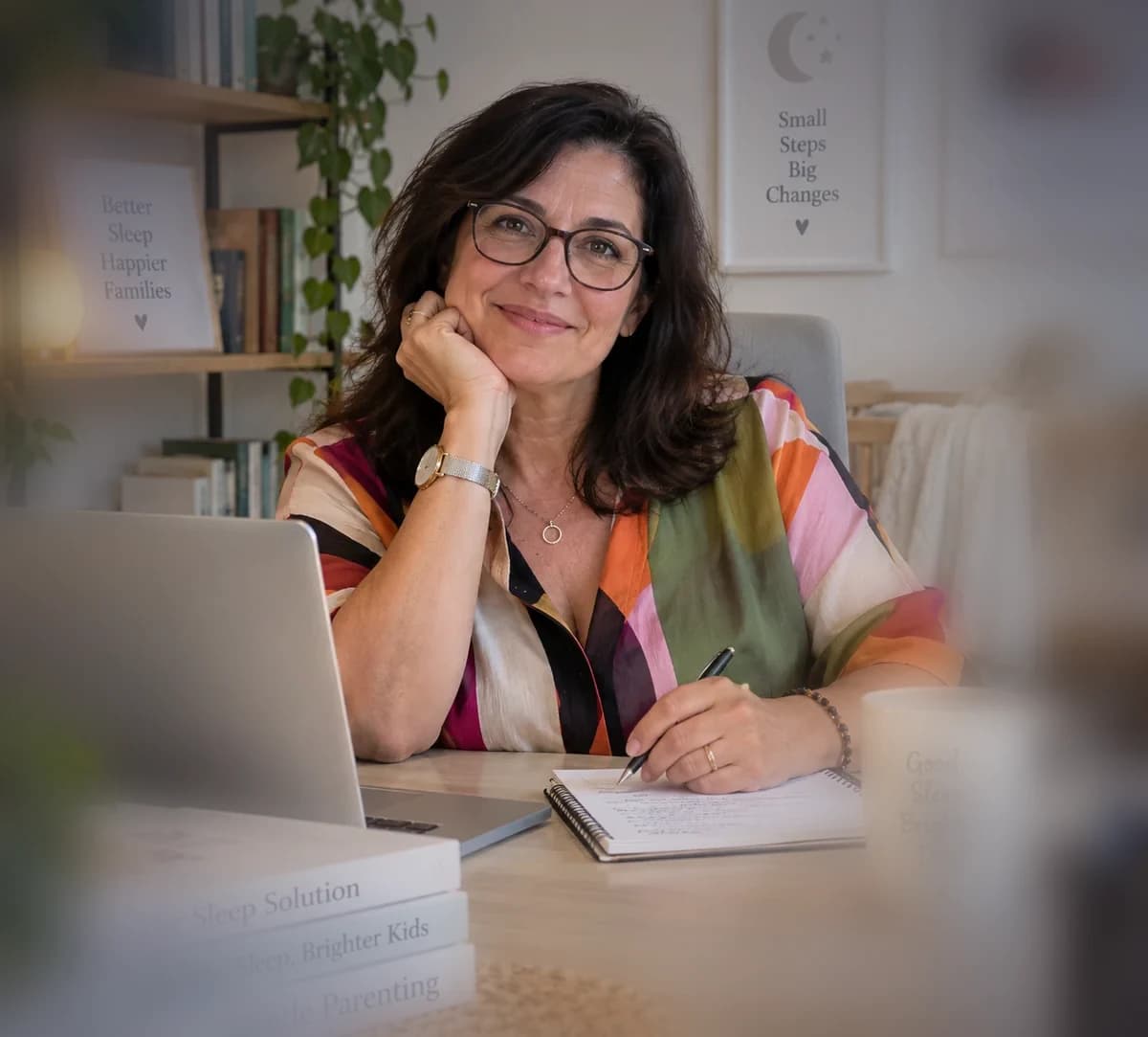 רונית שגיא, יועצת שינה, יושבת ליד שולחן העבודה עם מחשב ומחברת